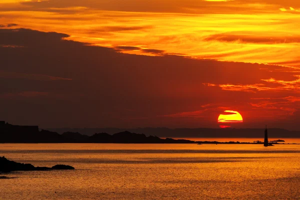 Pôr do sol ardente sobre o mar com um farol — Fotografia de Stock