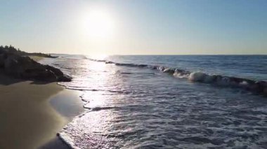 Ufukta parlak güneşle denize doğru ilerleyen hava aracı mavi okyanus suyu ve dalgaları üzerinden güneşe doğru uçan sinematik dron. Yüksek kalite 4k görüntü