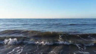 Sakin okyanus dalgaları berrak mavi bir gökyüzü altında yavaşça hareket ederken okyanusta temiz gökyüzü görüşü ile akan mavi dalgalar. Yüksek kalite 4k görüntü