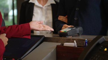 Müşteri otel resepsiyonunda kredi kartı terminalini kullanarak ödeme yapıyor, işlem sürecini kapatıyor