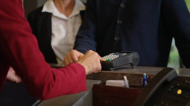 Müşteri otel resepsiyonunda kredi kartı terminalini kullanarak ödeme yapıyor, işlem sürecini kapatıyor