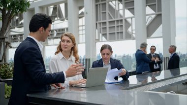 Modern bir çatıdaki açık hava toplantısında iş ekibi dizüstü bilgisayarda birlikte çalışıyor.