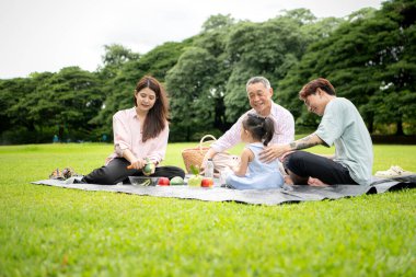 Mutlu Asyalı nesiller parkta pikniğin tadını çıkararak neşeli bir açık hava yaşam tarzı yaratıyor.