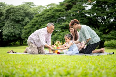 Mutlu Asyalı nesiller parkta pikniğin tadını çıkararak neşeli bir açık hava yaşam tarzı yaratıyor.