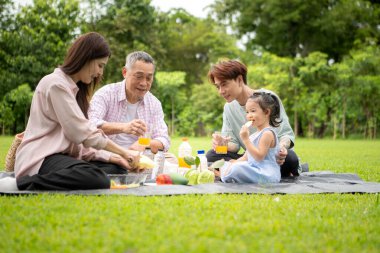 Mutlu Asyalı nesiller parkta pikniğin tadını çıkararak neşeli bir açık hava yaşam tarzı yaratıyor.