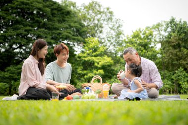Mutlu Asyalı nesiller parkta pikniğin tadını çıkararak neşeli bir açık hava yaşam tarzı yaratıyor.