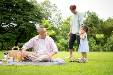 Mutlu Asyalı nesiller parkta pikniğin tadını çıkararak neşeli bir açık hava yaşam tarzı yaratıyor.