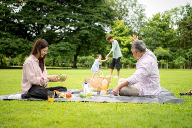 Mutlu Asyalı nesiller parkta pikniğin tadını çıkararak neşeli bir açık hava yaşam tarzı yaratıyor.