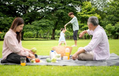 Mutlu Asyalı nesiller parkta pikniğin tadını çıkararak neşeli bir açık hava yaşam tarzı yaratıyor.