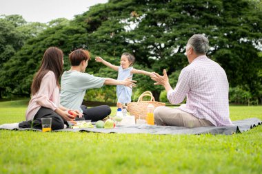 Mutlu Asyalı nesiller parkta pikniğin tadını çıkararak neşeli bir açık hava yaşam tarzı yaratıyor.