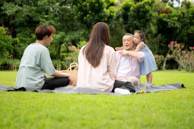 Mutlu Asyalı nesiller parkta pikniğin tadını çıkararak neşeli bir açık hava yaşam tarzı yaratıyor.