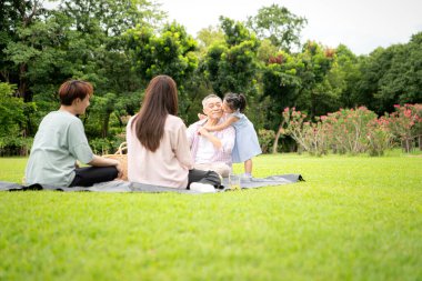 Mutlu Asyalı nesiller parkta pikniğin tadını çıkararak neşeli bir açık hava yaşam tarzı yaratıyor.