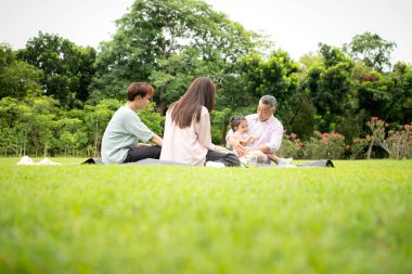 Mutlu Asyalı nesiller parkta pikniğin tadını çıkararak neşeli bir açık hava yaşam tarzı yaratıyor.