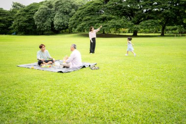 Mutlu Asyalı nesiller parkta pikniğin tadını çıkararak neşeli bir açık hava yaşam tarzı yaratıyor.