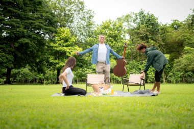 Mutlu Asyalı nesiller parkta pikniğin tadını çıkartıyor büyükbabam gitar çalıyor neşeli bir açık hava hayatı yaratıyor.