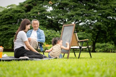 Mutlu Asyalı nesiller parkta pikniğin tadını çıkartıyor büyükbabam gitar çalıyor neşeli bir açık hava hayatı yaratıyor.