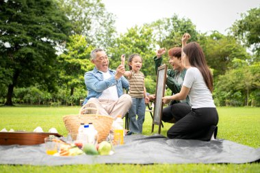 Mutlu Asyalı nesiller parkta pikniğin tadını çıkartıyor büyükbabam gitar çalıyor neşeli bir açık hava hayatı yaratıyor.