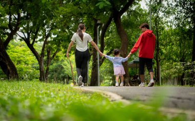 Asyalı bir aile parkta birlikte koşuyor. Ebeveynler ve kızları dışarıda egzersiz yapıyor, sağlıklı yaşam tarzını ve aile bağlarını destekliyor.