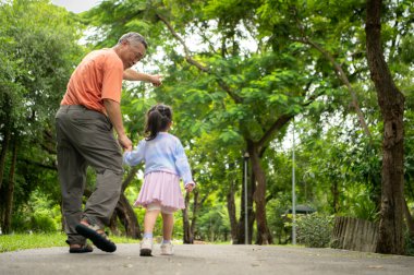 Büyükbaba ve torun parkta birlikte koşuyorlar, sağlıklı yaşam tarzını ve aile bağlarını destekliyorlar.
