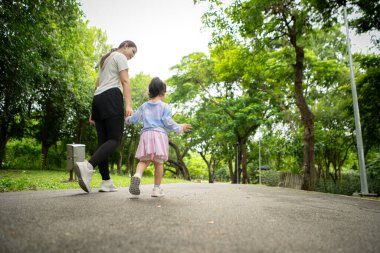 Anne ve kızı parkta birlikte koşuyor, sağlıklı yaşam tarzını ve aile bağlarını destekliyor.