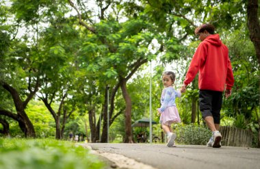 Baba ve kızı parkta birlikte koşuyor, sağlıklı yaşam tarzını ve aile bağlarını destekliyor.