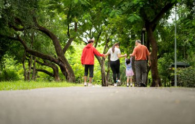 Asyalı bir aile parkta birlikte koşuyor. Ebeveynler, çocuklar ve büyükbabalar dışarıda egzersiz yapıyor, sağlıklı yaşam tarzını ve aile bağlarını destekliyor.