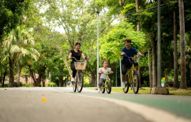 Ebeveynler ve küçük kız tatillerde parkta dengeli bisiklet sürerler.
