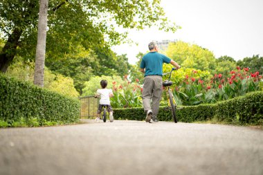 Büyükbaba ve küçük kız tatillerde parkta dengeli bisiklete binecekler.