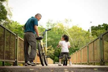 Büyükbaba ve küçük kız tatillerde parkta dengeli bisiklete binecekler.