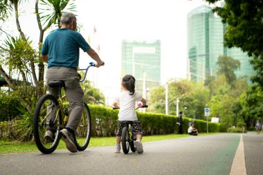 Büyükbaba ve küçük kız tatillerde parkta dengeli bisiklete binecekler.