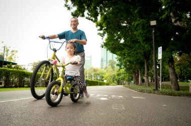 Büyükbaba ve küçük kız tatillerde parkta dengeli bisiklete binecekler.