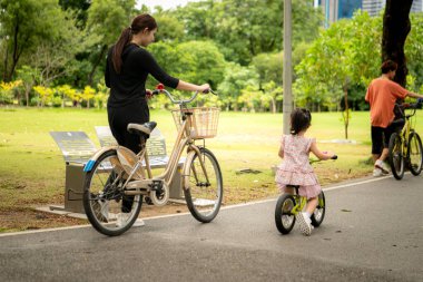 Ebeveynler ve küçük kız tatillerde parkta dengeli bisiklet sürerler.