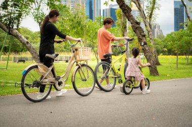 Ebeveynler ve küçük kız tatillerde parkta dengeli bisiklet sürerler.
