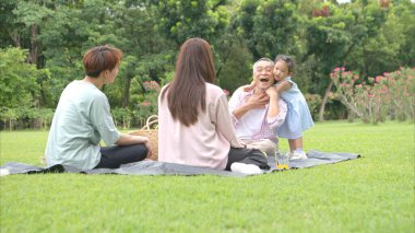 Mutlu Asyalı nesiller parkta pikniğin tadını çıkararak neşeli bir açık hava yaşam tarzı yaratıyor.