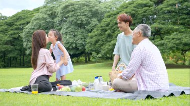 Mutlu Asyalı nesiller parkta pikniğin tadını çıkararak neşeli bir açık hava yaşam tarzı yaratıyor.