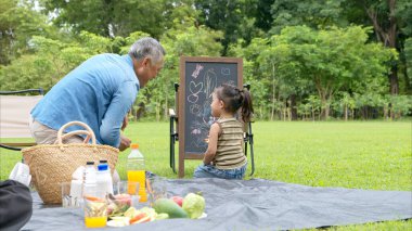 Mutlu Asyalı nesiller parkta pikniğin tadını çıkartıyor büyükbabam gitar çalıyor neşeli bir açık hava hayatı yaratıyor.