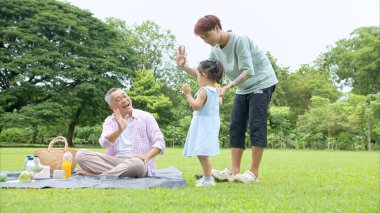 Mutlu Asyalı nesiller parkta pikniğin tadını çıkararak neşeli bir açık hava yaşam tarzı yaratıyor.