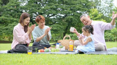 Mutlu Asyalı nesiller parkta pikniğin tadını çıkararak neşeli bir açık hava yaşam tarzı yaratıyor.