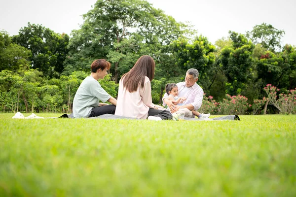 Mutlu Asyalı nesiller parkta pikniğin tadını çıkararak neşeli bir açık hava yaşam tarzı yaratıyor.