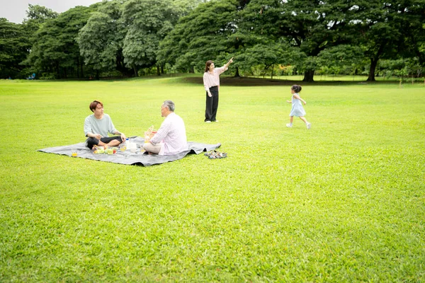 Mutlu Asyalı nesiller parkta pikniğin tadını çıkararak neşeli bir açık hava yaşam tarzı yaratıyor.