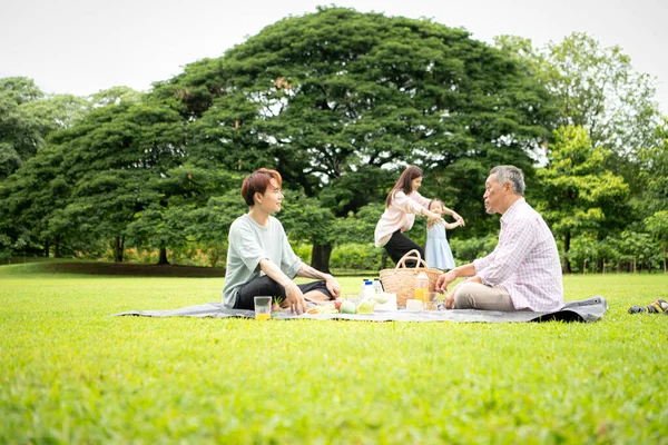 Mutlu Asyalı nesiller parkta pikniğin tadını çıkararak neşeli bir açık hava yaşam tarzı yaratıyor.
