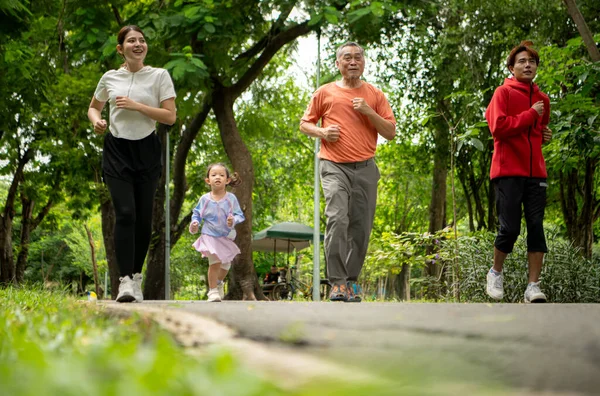 Asyalı bir aile parkta birlikte koşuyor. Ebeveynler, çocuklar ve büyükbabalar dışarıda egzersiz yapıyor, sağlıklı yaşam tarzını ve aile bağlarını destekliyor.