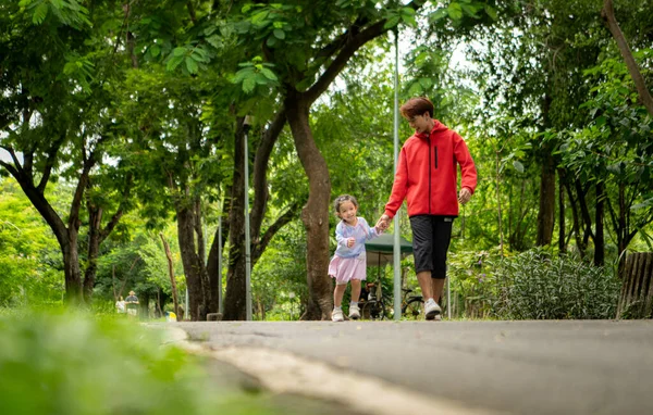 Baba ve kızı parkta birlikte koşuyor, sağlıklı yaşam tarzını ve aile bağlarını destekliyor.