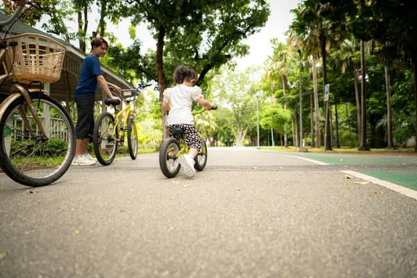 Ebeveynler ve küçük kız tatillerde parkta dengeli bisiklet sürerler.
