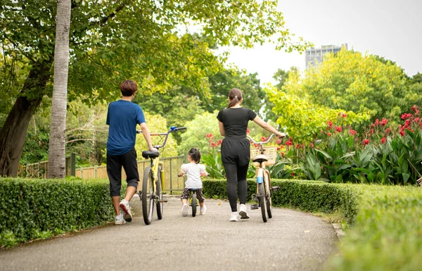 Ebeveynler ve küçük kız tatillerde parkta dengeli bisiklet sürerler.