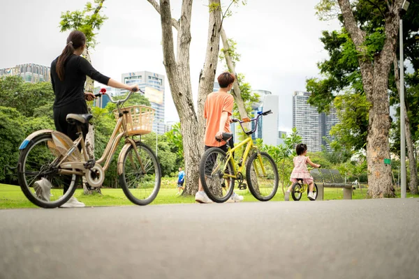 Ebeveynler ve küçük kız tatillerde parkta dengeli bisiklet sürerler.