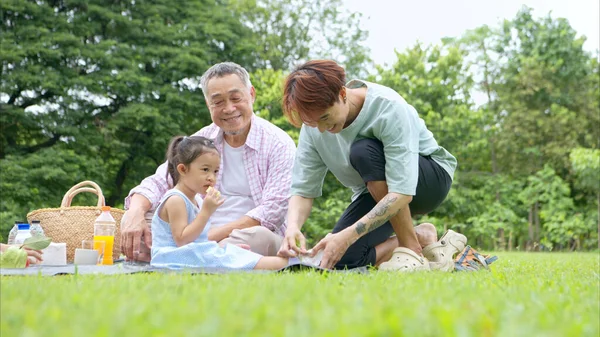 Mutlu Asyalı nesiller parkta pikniğin tadını çıkararak neşeli bir açık hava yaşam tarzı yaratıyor.