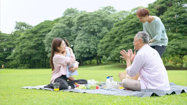 Mutlu Asyalı nesiller parkta pikniğin tadını çıkararak neşeli bir açık hava yaşam tarzı yaratıyor.