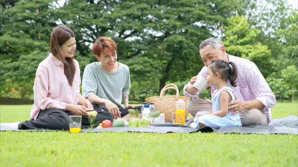 Mutlu Asyalı nesiller parkta pikniğin tadını çıkararak neşeli bir açık hava yaşam tarzı yaratıyor.