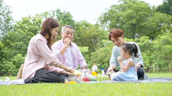 Mutlu Asyalı nesiller parkta pikniğin tadını çıkararak neşeli bir açık hava yaşam tarzı yaratıyor.